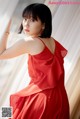 A woman in a red dress leaning against a window.