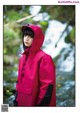 A woman in a red raincoat standing in front of a waterfall.