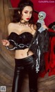 A woman in a black top and leather pants holding a knife.