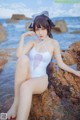 A woman in a white bathing suit sitting on a rock by the ocean.