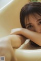 A woman sitting in a bathtub with her hand on her face.