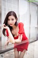 A woman in a red dress leaning against a glass wall.