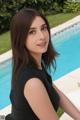 A woman in a black dress sitting by a swimming pool.